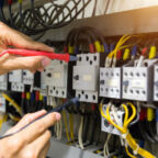 Electricians hands testing current electric in control panel.